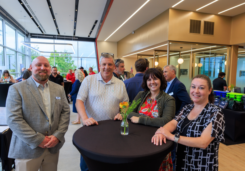 Four people posing and smiling around a table at Flow Kia of Charlottesville