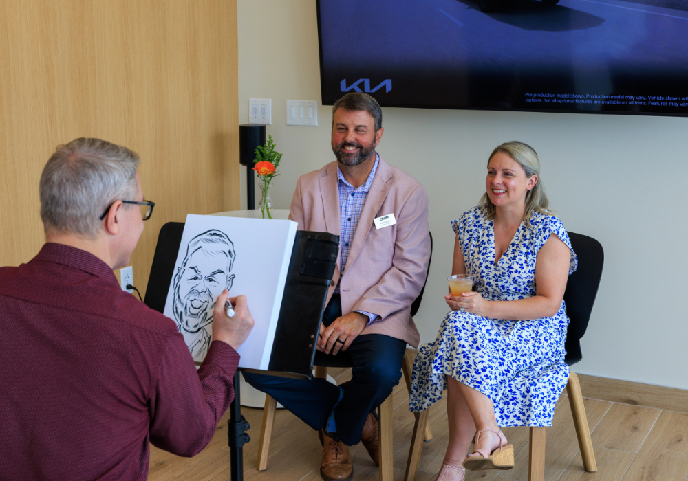 A man and a woman having their caricature drawn inside Flow Kia of Charlottesville