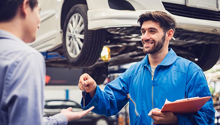 Smiling mechanic in blue coveralls returns car keys to a customer.