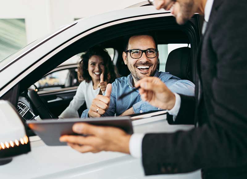 A happy couple gives a thumbs-up from inside their new car