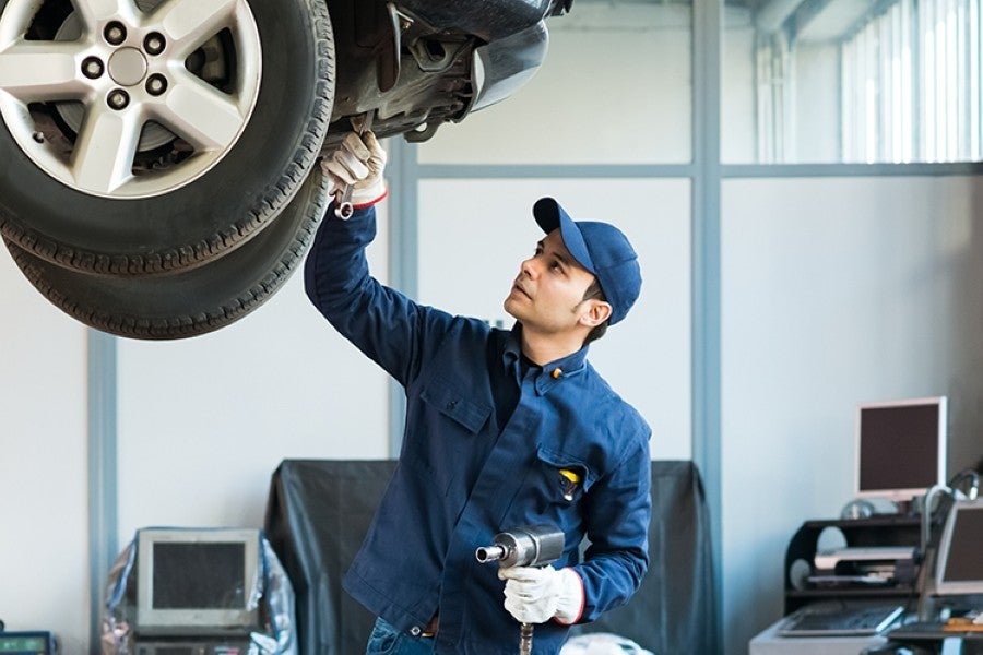 A mechanic in a blue uniform inspects a car on a lift.